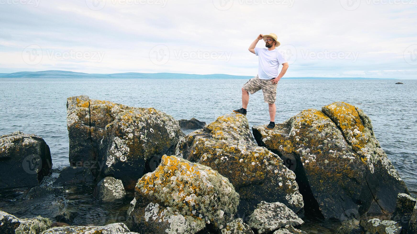 Handsome bearded man with straw hat standing on the rocks by the ocean at wild Atlantic way, adventure and lifestyle concept, summer, vacation, nature background photo