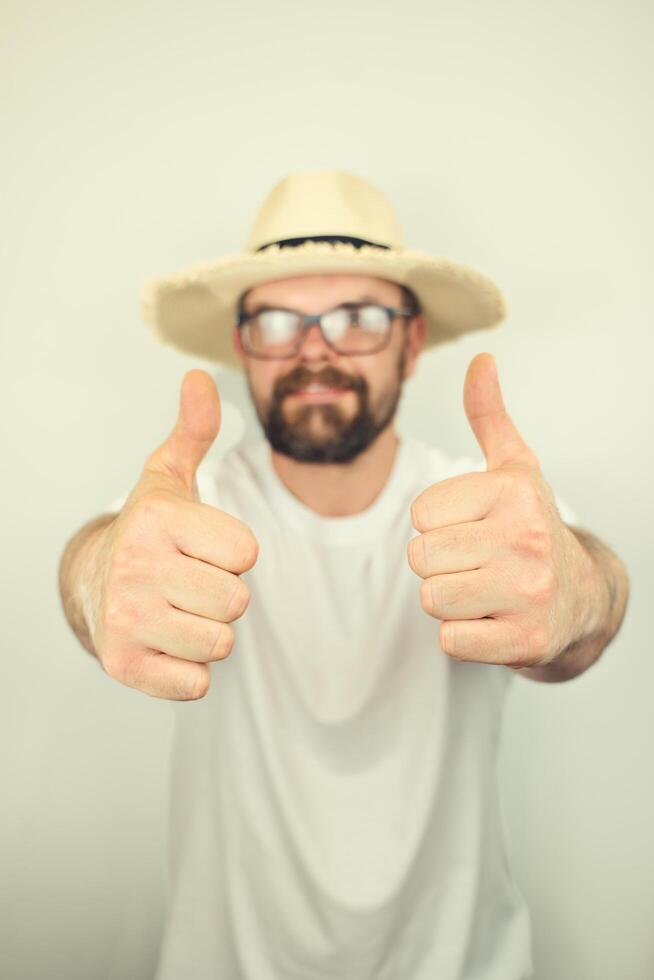 portrait of handsome bearded man with straw hat and glasses smiling, thumbs up gesture, wearing white shirt , isolated on white background photo