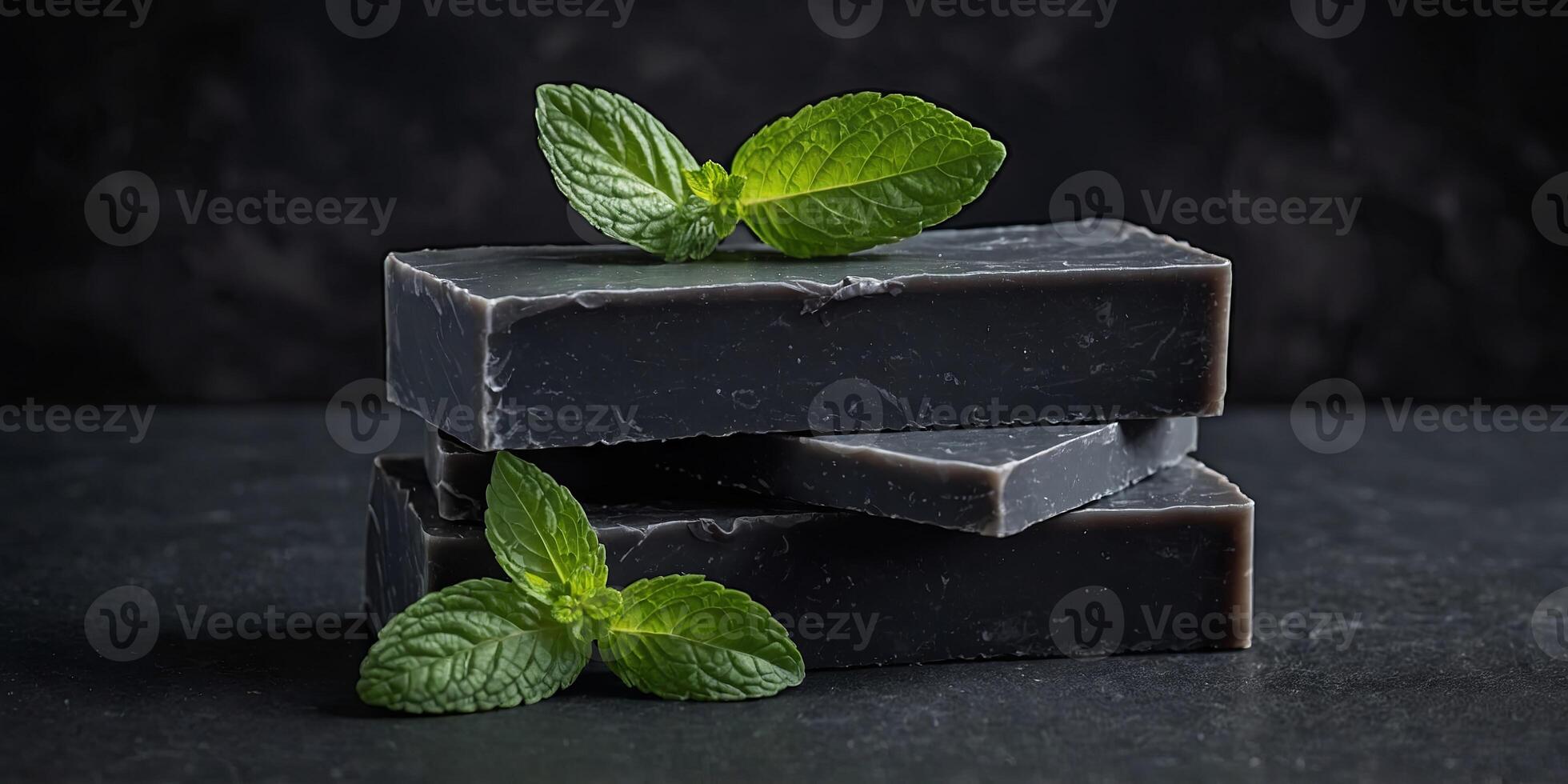 Stacked charcoal soap bars garnished with fresh mint leaves, presented on a dark slate background for a clean and modern aesthetic. photo