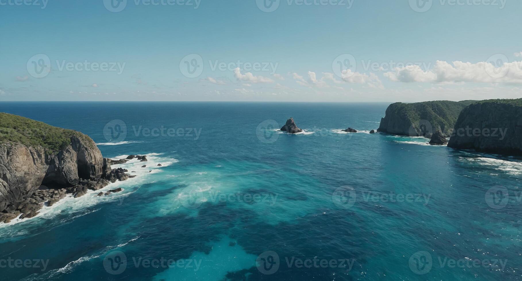 A serene ocean view from a high vantage point, showcasing calm, turquoise waters extending to the horizon under a light blue sky Rocky outcrops are visible near the bottom of the image. photo