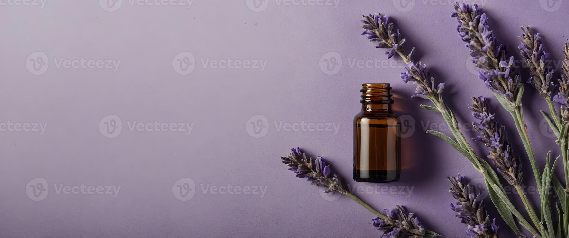 A bottle of essential oil nestled among lavender stems on a soft purple background, presented in a flat lay composition from a top view perspective. photo