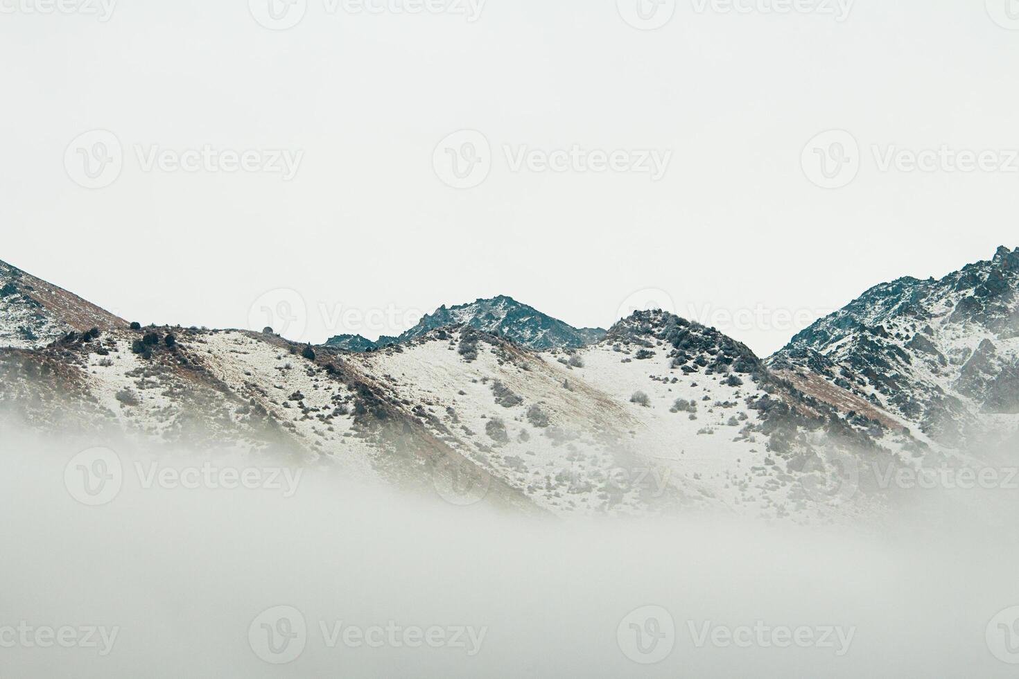View of majestic mountain peaks with snow. Below there is fog and gray sky. Nature photo