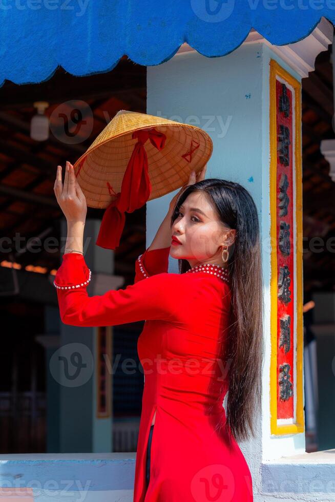 Vietnamese girl with Ao Dai dress standing in traditional house of Vietnam. Text in photo mean best wishes to family, happiness, prosperity, health. Tet holiday and New Year.