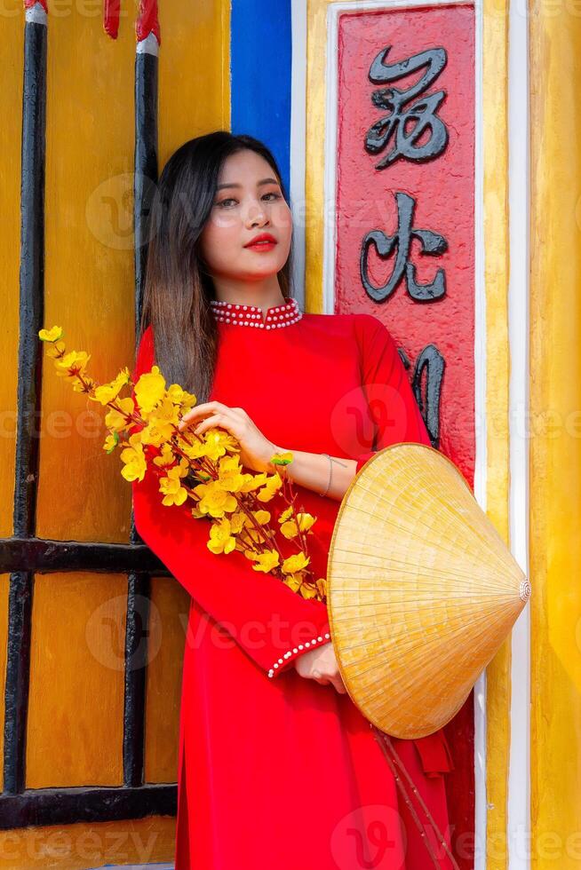 Vietnamese girl with Ao Dai dress standing in traditional house of Vietnam. Text in photo mean best wishes to family, happiness, prosperity, health. Tet holiday and New Year.