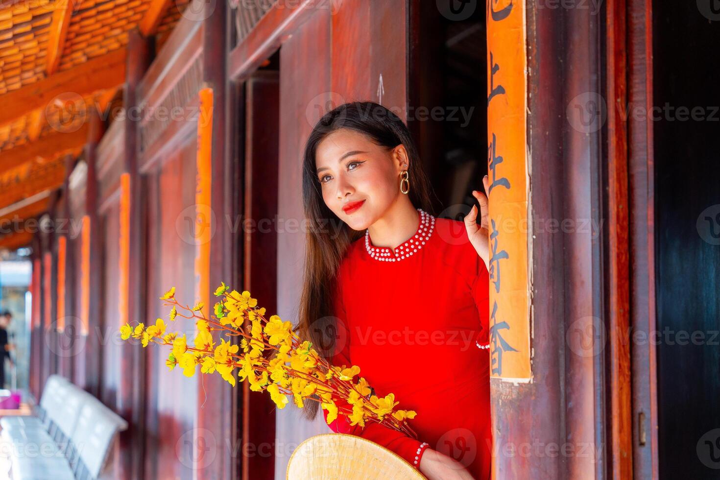 Vietnamese girl with Ao Dai dress standing in traditional house of Vietnam. Text in photo mean best wishes to family, happiness, prosperity, health. Tet holiday and New Year.