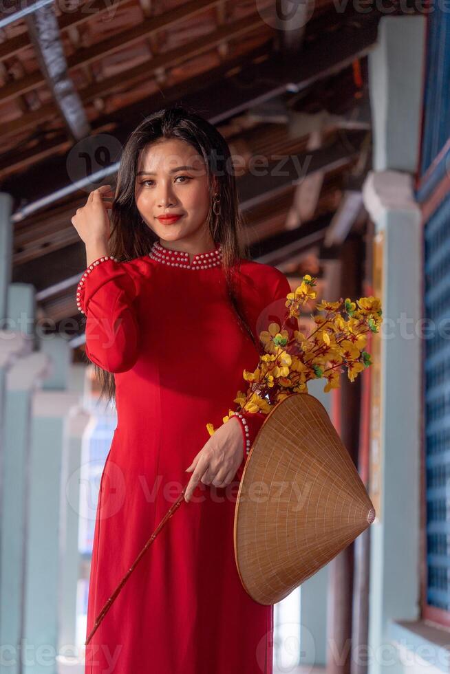 Vietnamese girl with Ao Dai dress standing in traditional house of Vietnam. Text in photo mean best wishes to family, happiness, prosperity, health. Tet holiday and New Year.
