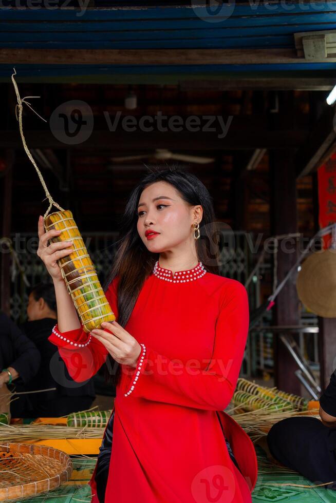 Vietnamese girl with Ao Dai dress sitting in traditional house of Vietnam and making Tet Cake, Tet food outdoor with old woman. Traditional Vietnamese New Year Tet food. photo