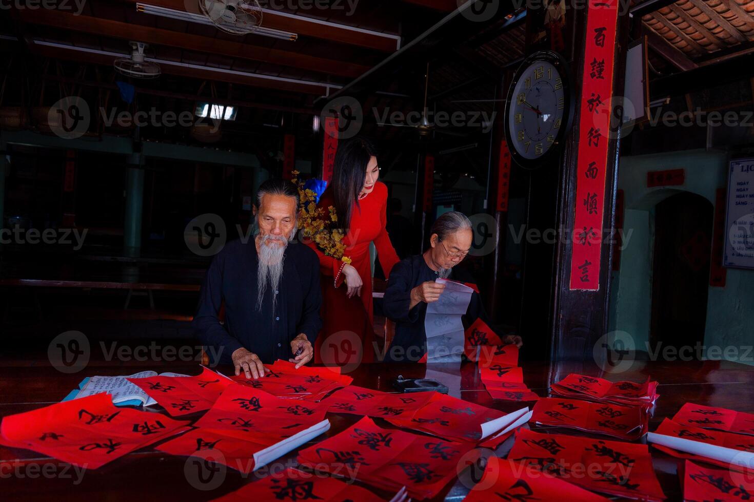 Vietnamese girl with red Ao Dai dress and old scholars writing calligraphy at lunar new year. Calligraphy is a popular tradition during Tet holiday. Text in photo mean Happy New Year and Peace.
