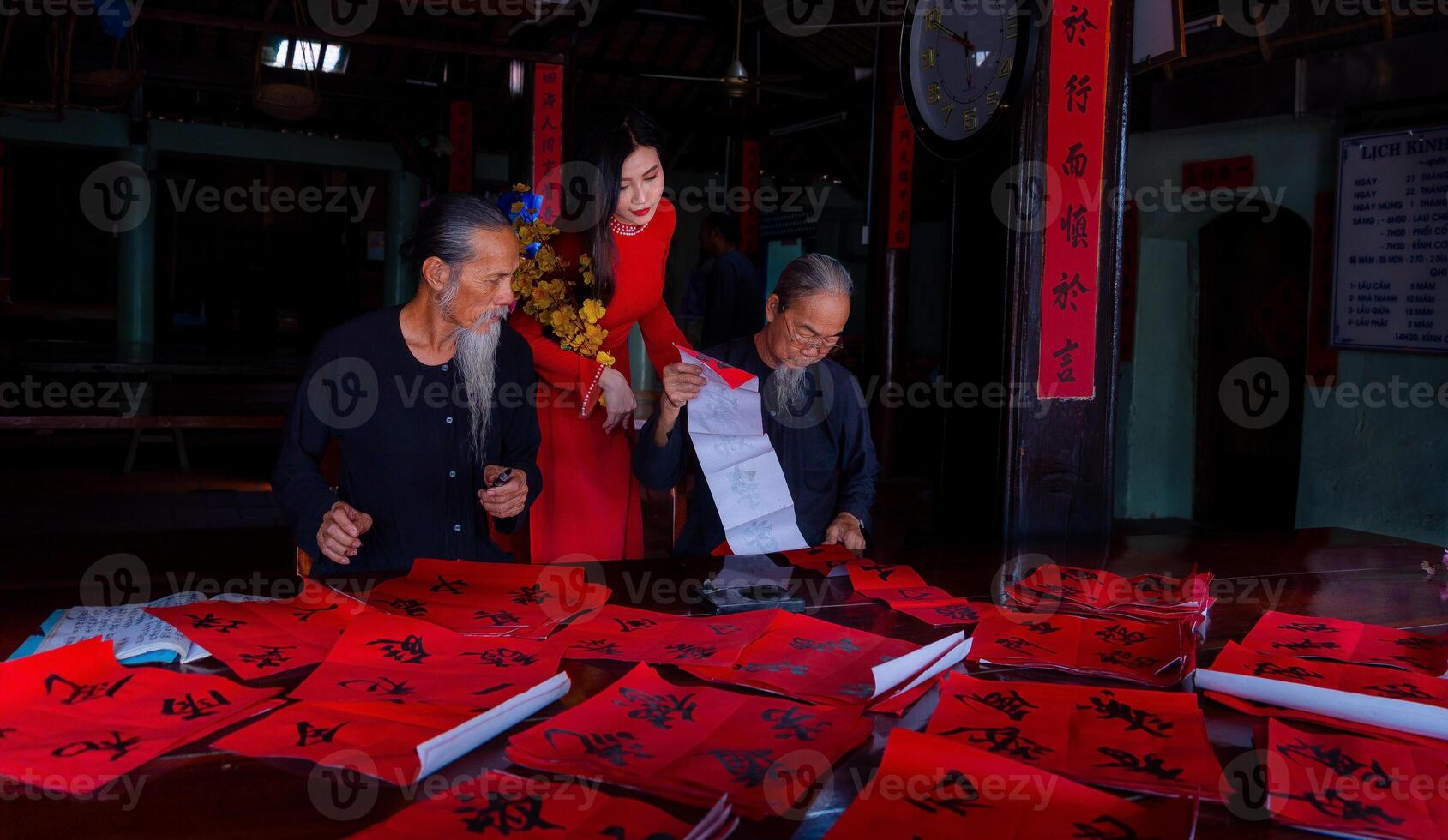 Vietnamese girl with red Ao Dai dress and old scholars writing calligraphy at lunar new year. Calligraphy is a popular tradition during Tet holiday. Text in photo mean Happy New Year and Peace.