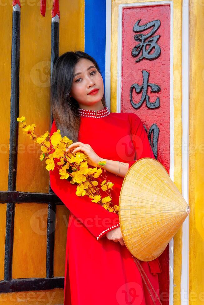 Vietnamese girl with Ao Dai dress standing in traditional house of Vietnam. Text in photo mean best wishes to family, happiness, prosperity, health. Tet holiday and New Year.