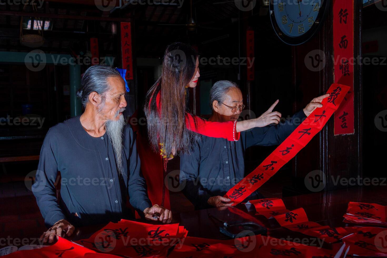 Vietnamese girl with red Ao Dai dress and old scholars writing calligraphy at lunar new year. Calligraphy is a popular tradition during Tet holiday. Text in photo mean Happy New Year and Peace.
