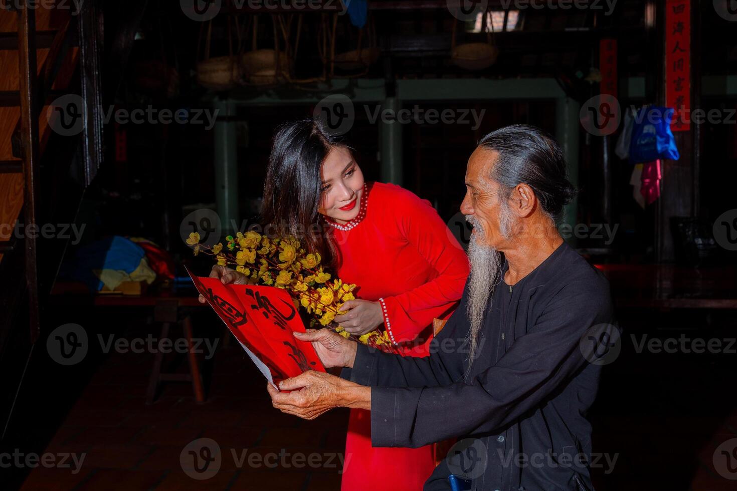 Vietnamese girl with red Ao Dai dress and old scholars writing calligraphy at lunar new year. Calligraphy is a popular tradition during Tet holiday. Text in photo mean Happy New Year and Peace.