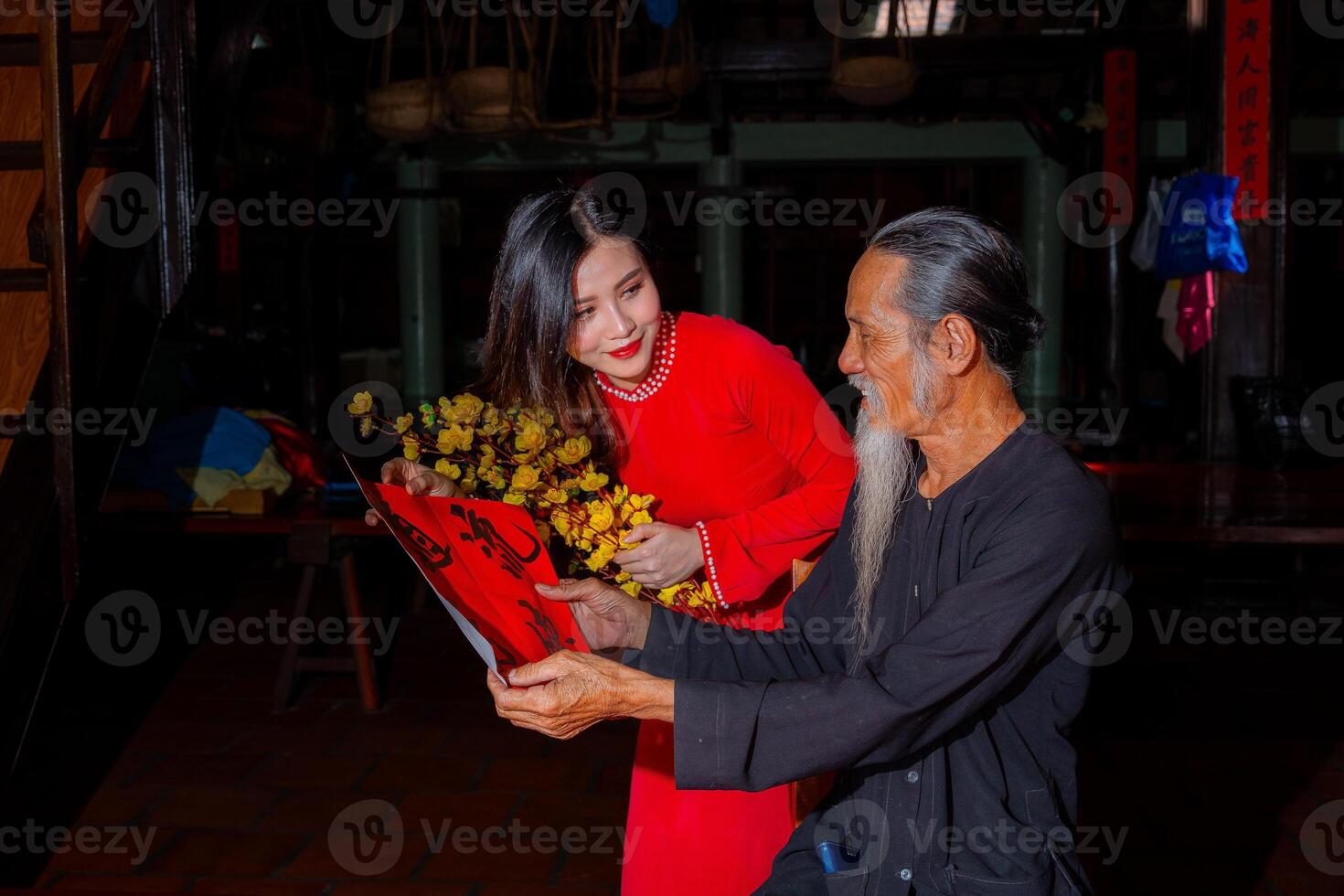 Vietnamese girl with red Ao Dai dress and old scholars writing calligraphy at lunar new year. Calligraphy is a popular tradition during Tet holiday. Text in photo mean Happy New Year and Peace.