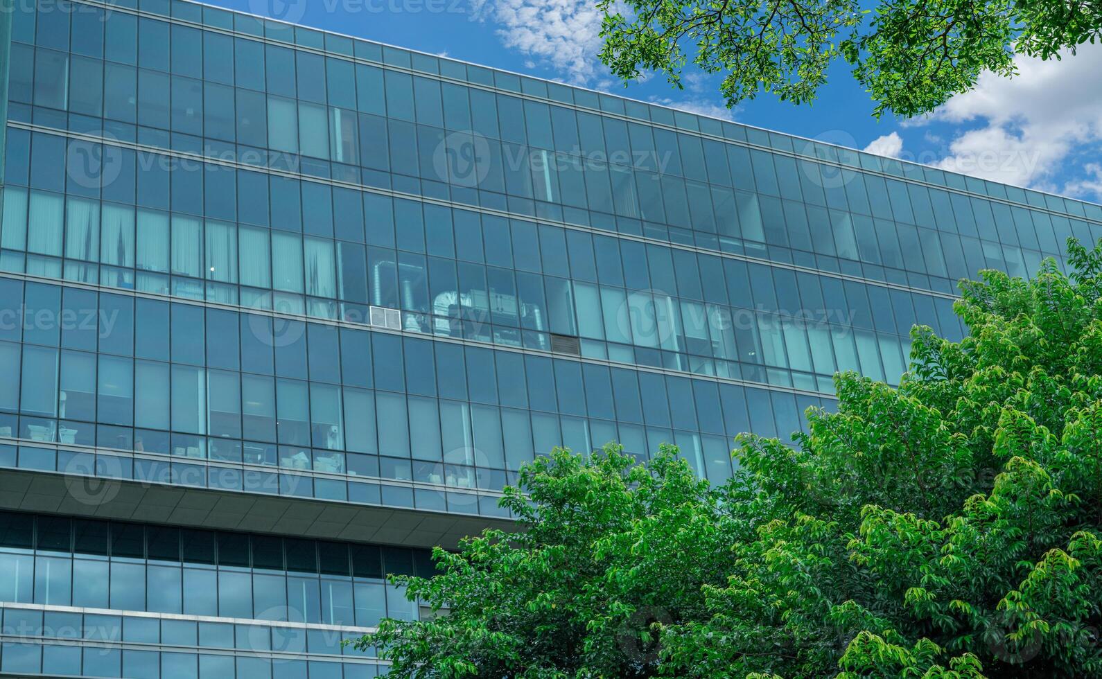 Eco-friendly building in modern city. Sustainable glass office building with trees for reducing carbon dioxide. Office building with green environment. Corporate building reduce CO2. Net zero emission photo