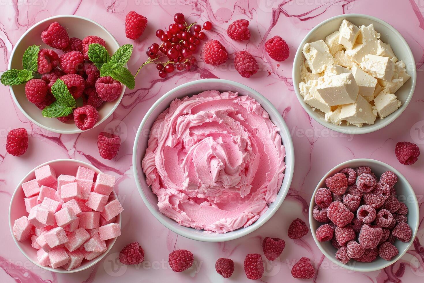 A bowl of pink frosting surrounded by raspberries red currants and pink sweets on a pink marbled surface photo