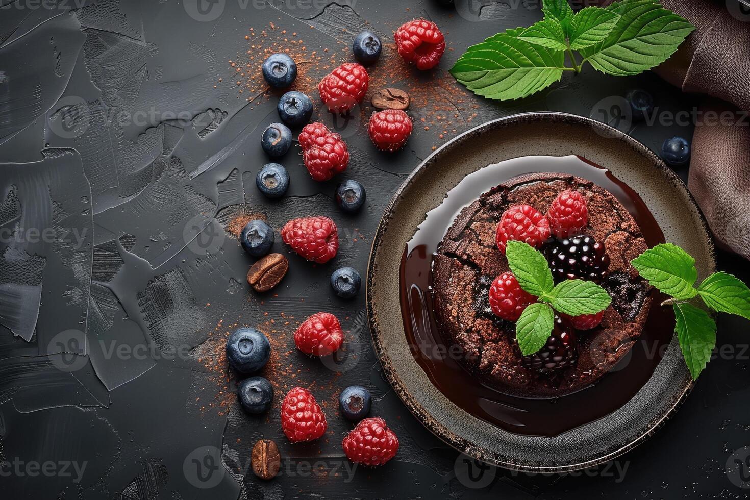 A chocolate cake topped with fresh raspberries blackberries and mint leaves resting on a dark plate with a chocolate sauce drizzle photo
