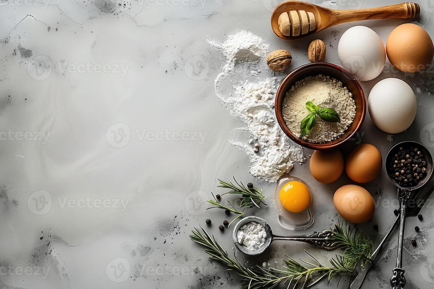 A scattering of ingredients for baking and cooking including flour eggs rosemary and peppercorns on a textured gray surface photo