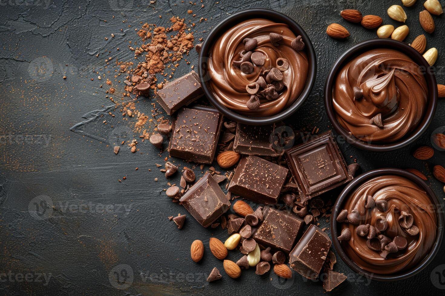 A dark rustic table scattered with chocolate squares chips and creamy swirls accented by almonds and hazelnut shells photo