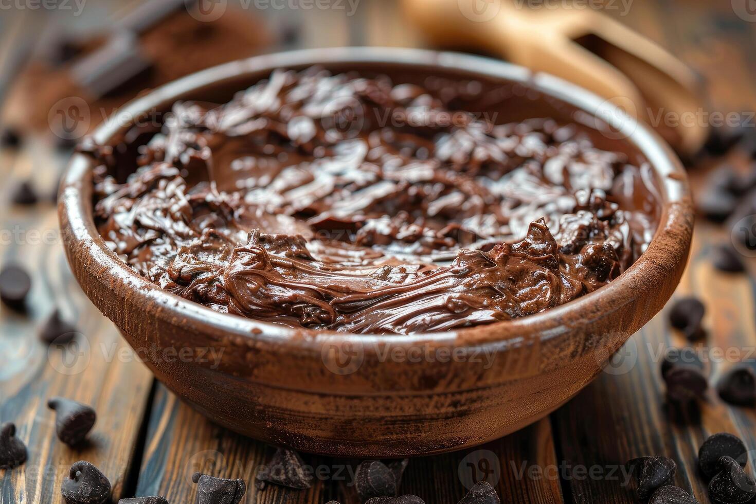 Melted chocolate in a wooden bowl with chocolate chips scattered on the table photo