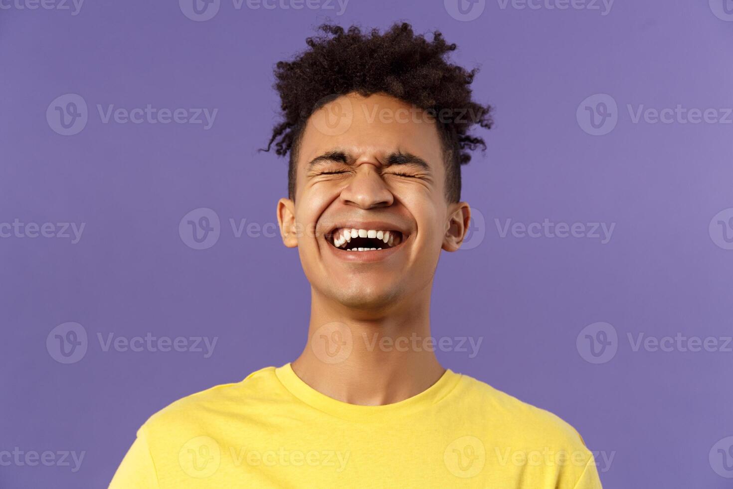 Close-up portrait of happy carefree young guy laughing loud, chuckling over hilarious joke, bending backwards and close eyes while giggle over funny movie, purple background photo