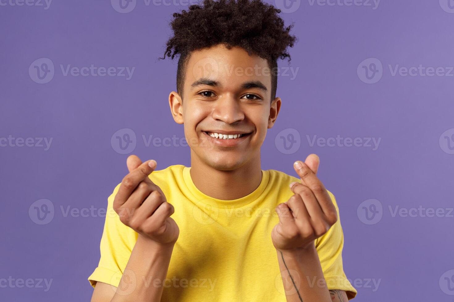 Close-up portrait of lovely cute young man with afro haircut, showing korean heart finger signs and smiling, express his love and sympathy towards person, stand purple background photo