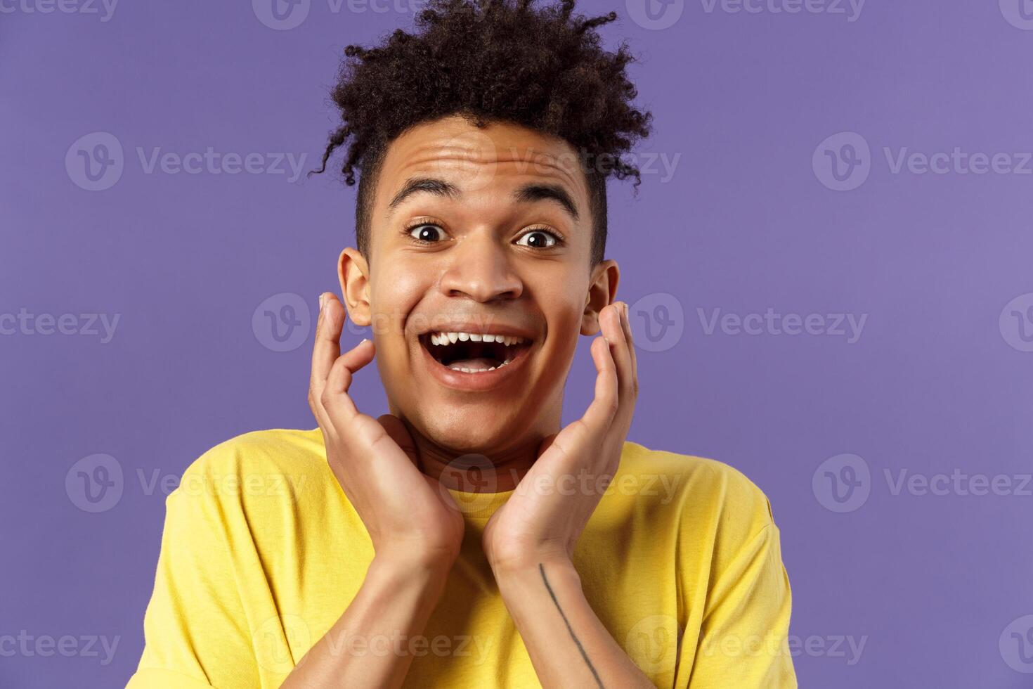 Close-up portrait of extremely happy, enthusiastic young man hear fantastic news, looking surprised and excited, touching face in joy, smiling upbeat look camera astonished, purple background photo