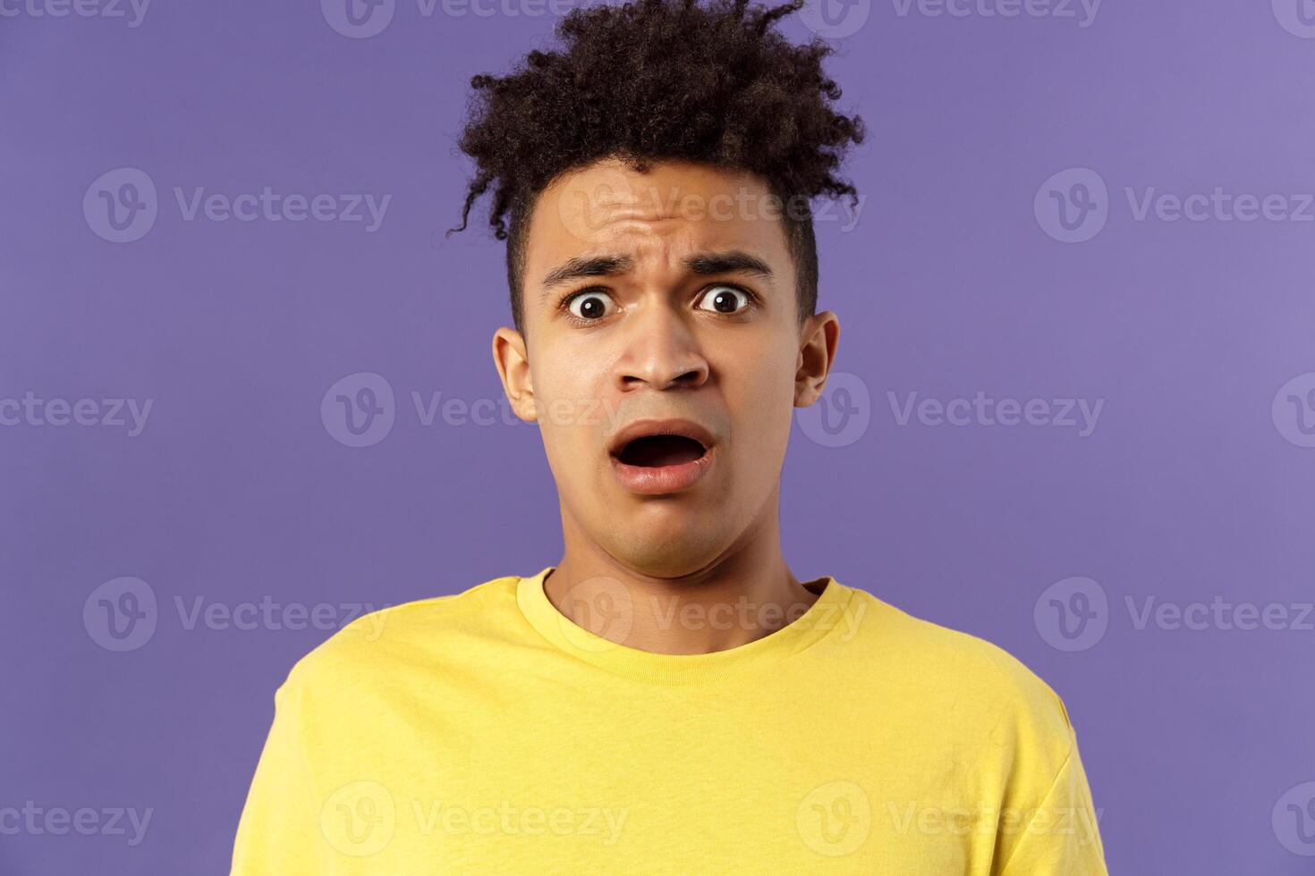 Close-up portrait of shocked, alarmed young man gasping, open mouth scared and frightened, staring camera concerned, facing troublesome shocking news, purple background photo