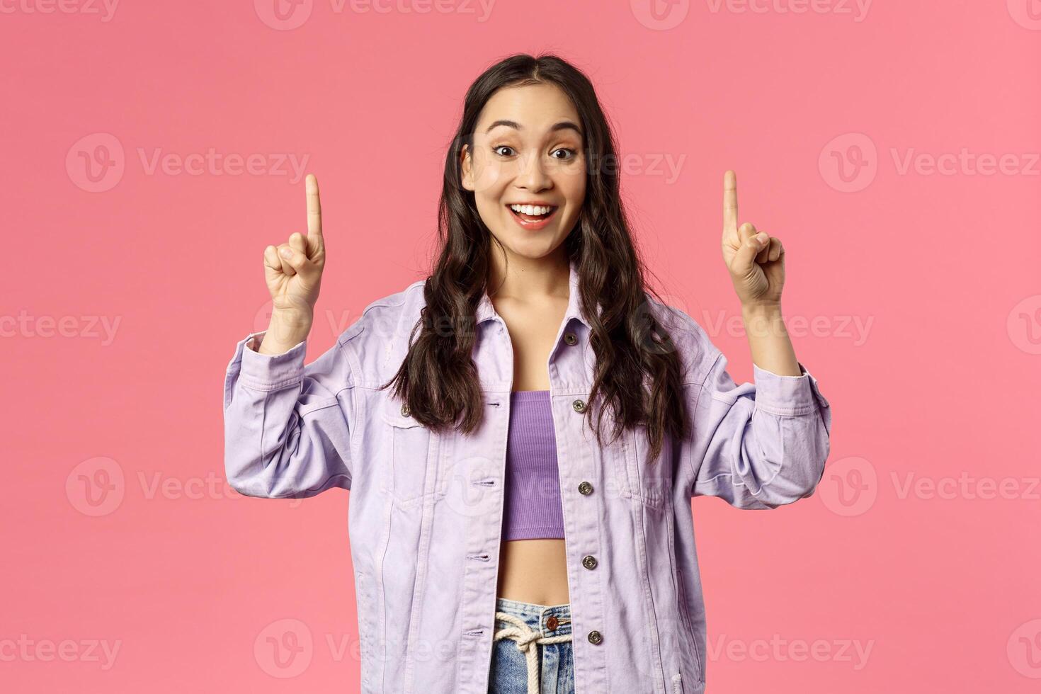 Lively attractive young brunette girl in denim jacket over crop-top asking you follow page, visit store or click link, recommend advertisement promo, smiling enthusiastic, pink background photo
