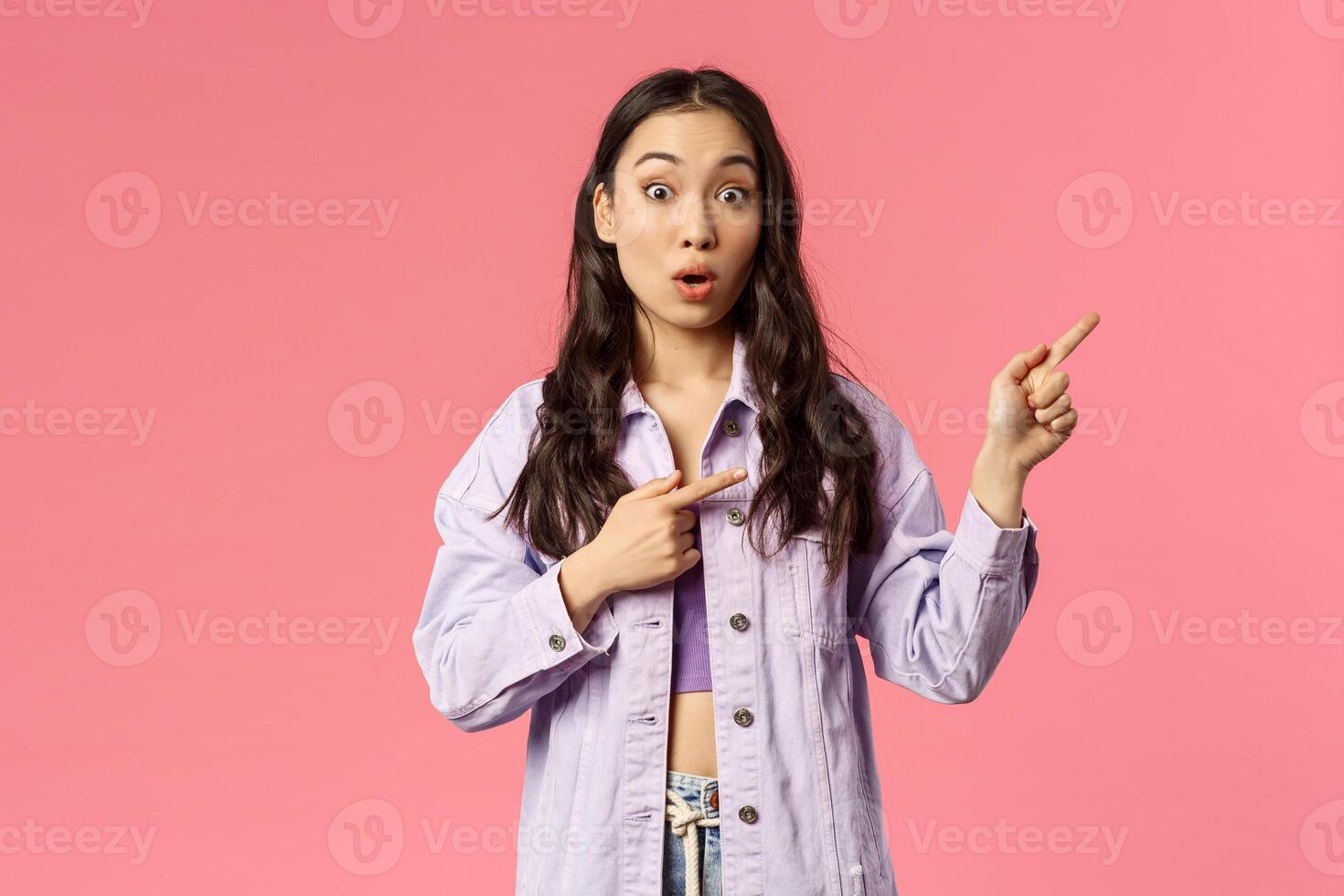 Have you seen it. Intrigued and curious attractive korean girl pointing fingers upper right corner and look camera with popped eyes, open mouth asking question about promo, pink background photo