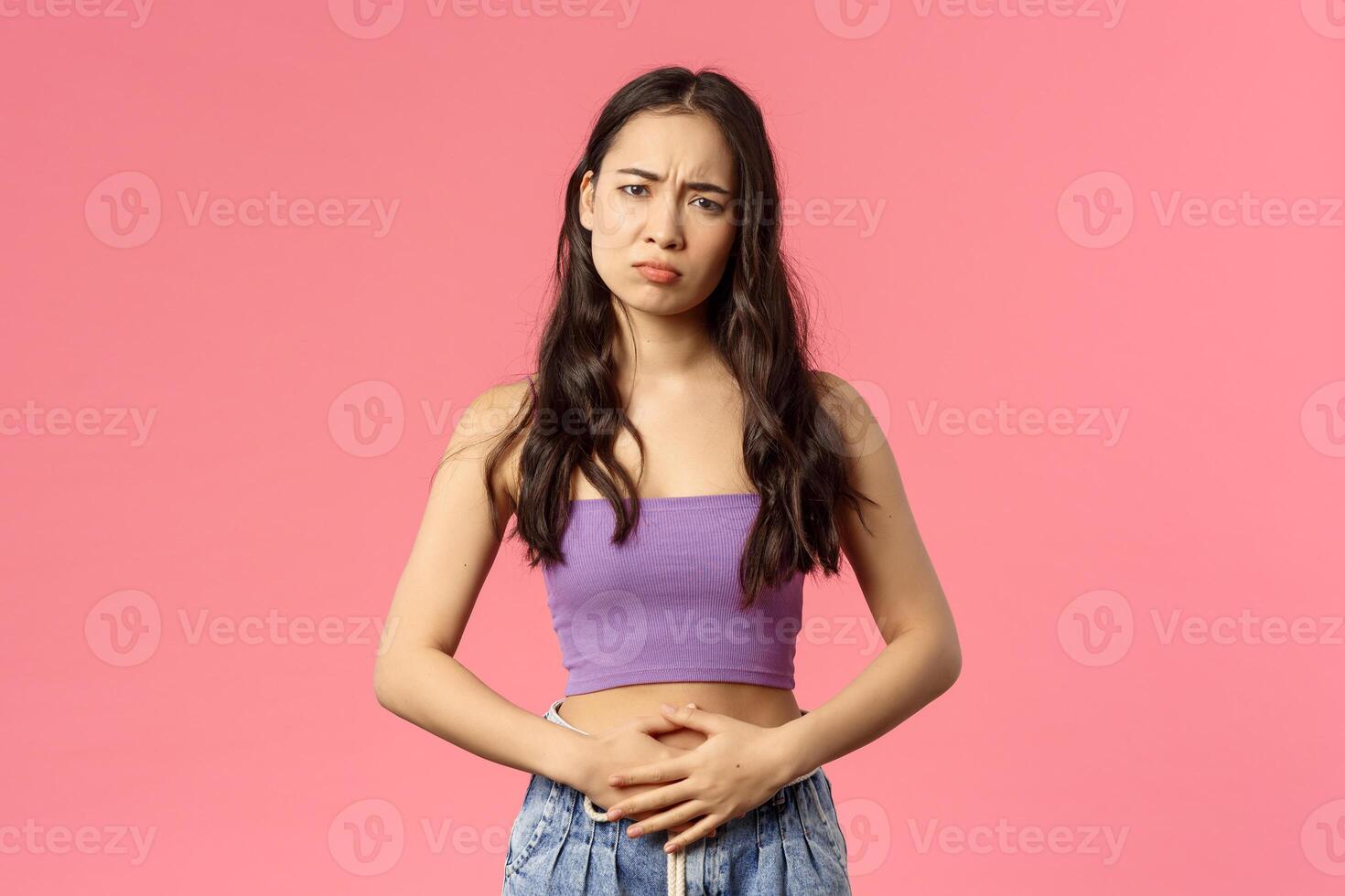 Health, medicine and people concept. Young stylish girl dressed-up for party but started feel pain in stomach, stomachache or menstrual cramps, gloomy looking camera as complaining, pink background photo
