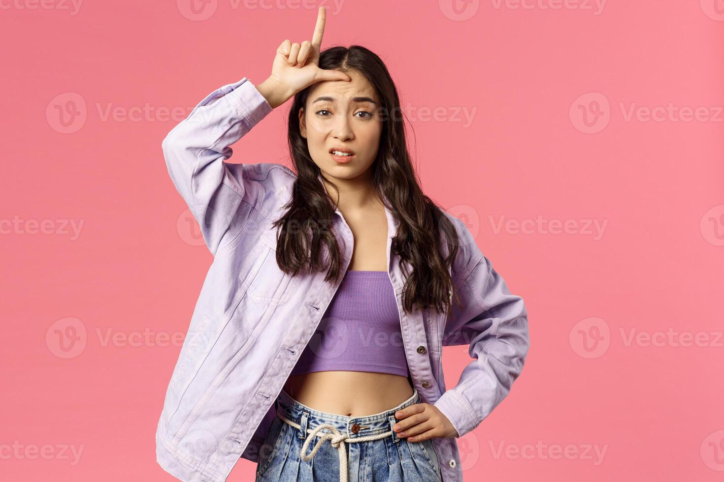Arrogant girl think someone not worth her attention. Portrait of populat female student make L letter on forehead as mocking person who lost, being cruel to loser, pink background photo