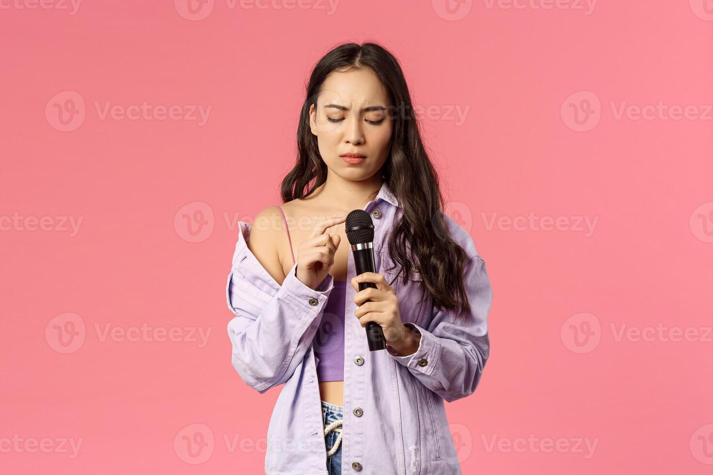 Portrait of awkward silly asian girl tap microphone as checking is it working, her turn to sing song on karaoke party, frowning complicated, standing pink background unsure how this thing works photo