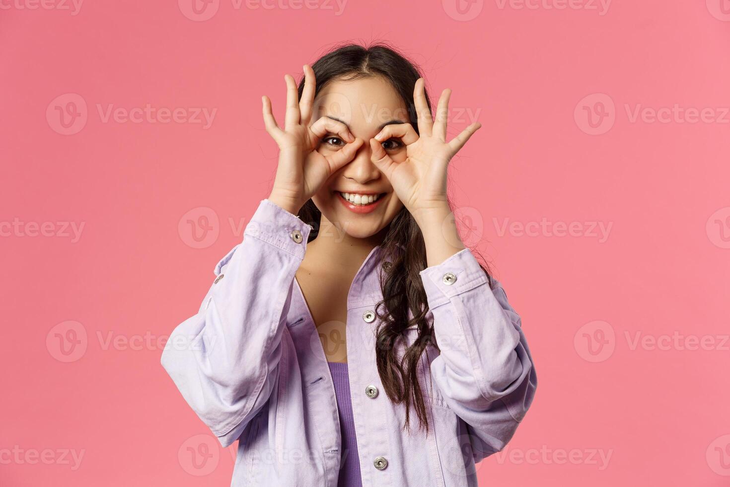 Close-up portrait of charismatic, funny and cute carefree teenage asian girl, making mask with fingers over eyes, smiling and looking camera, having fun, fool around and playing cheerful photo