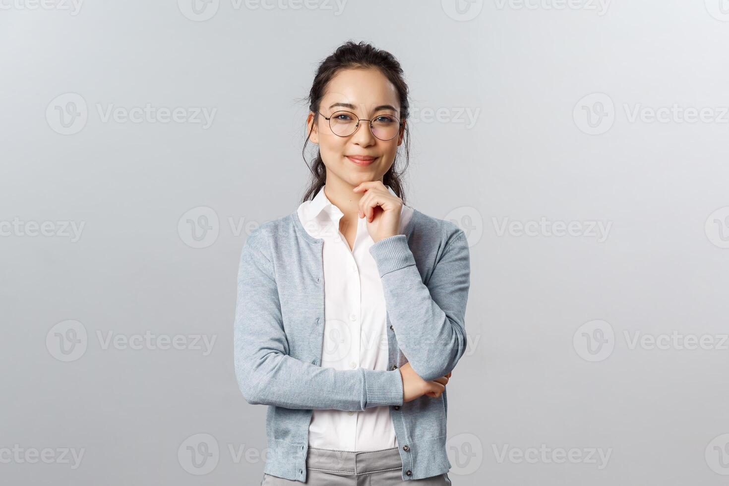 Hmm very interesting. Portrait of intrigued cute asian woman making choice, deciding between variants, look camera satisfied and smile, made-up plan, listening to curious suggestion, grey background photo