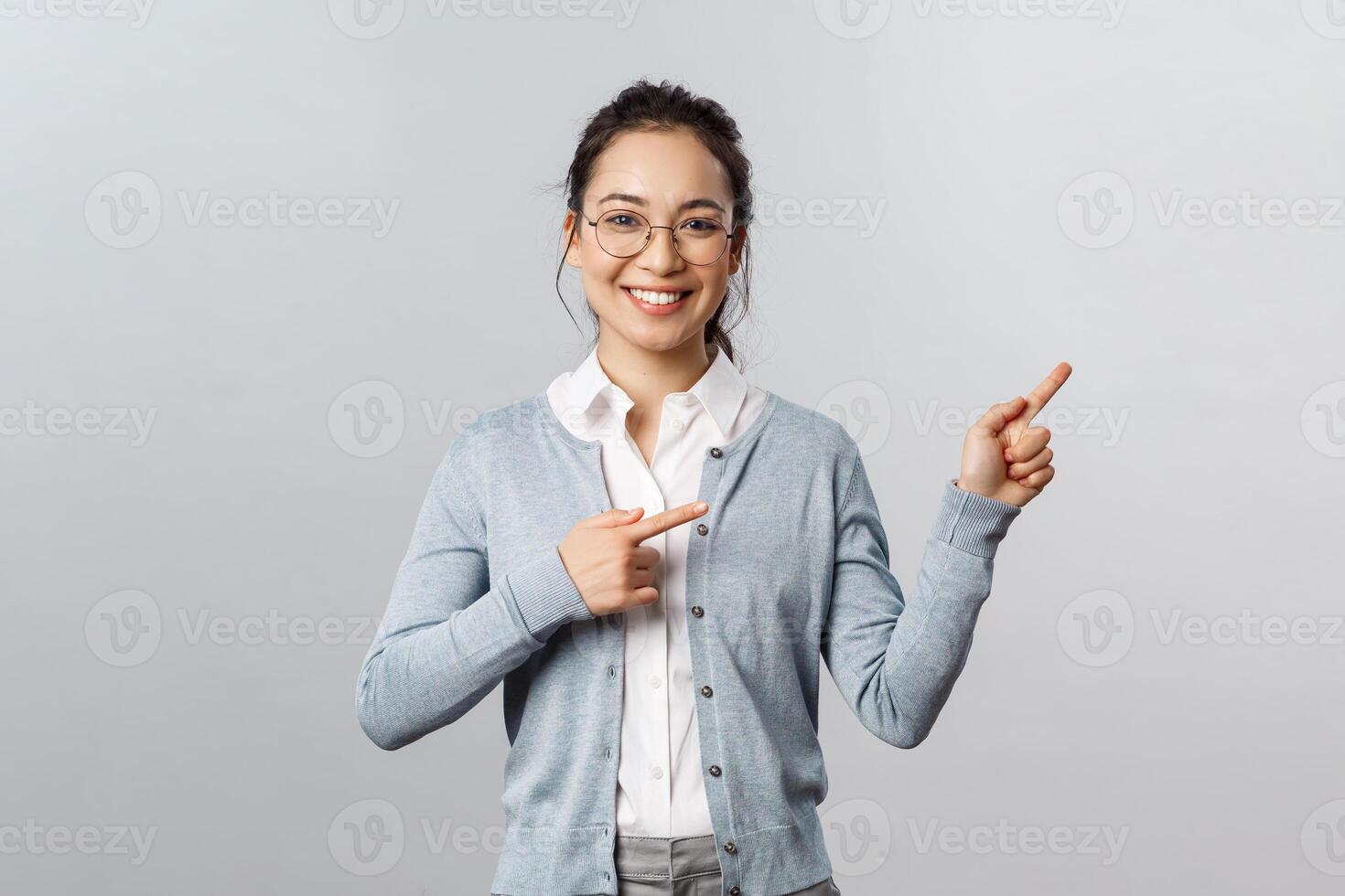 Education, studying and online classes concept. Cheerful asian woman, teacher pointing fingers right at presentation or chart, smiling friendly, helping find way, showing promo, grey background photo