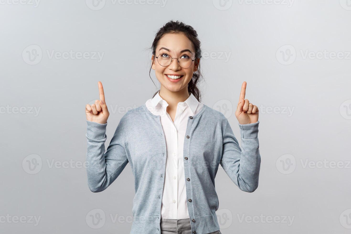 Extremely good news, cant wait to try it. Excited asian girl cant resist temptation, pointing fingers up, looking with interest and desire to try at top advertisement, standing grey background photo