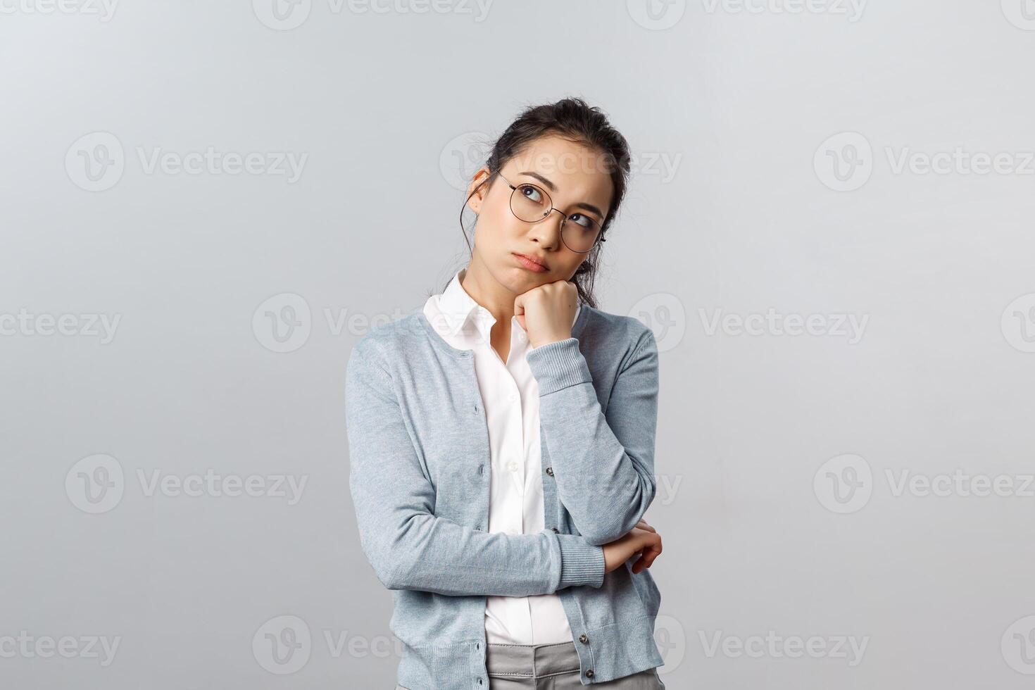 Portrait of bored and tired, thoughtful asian female employer dreaming about home, want go back early from office, looking up dreamy, thinking making plan, use imagination, grey background photo