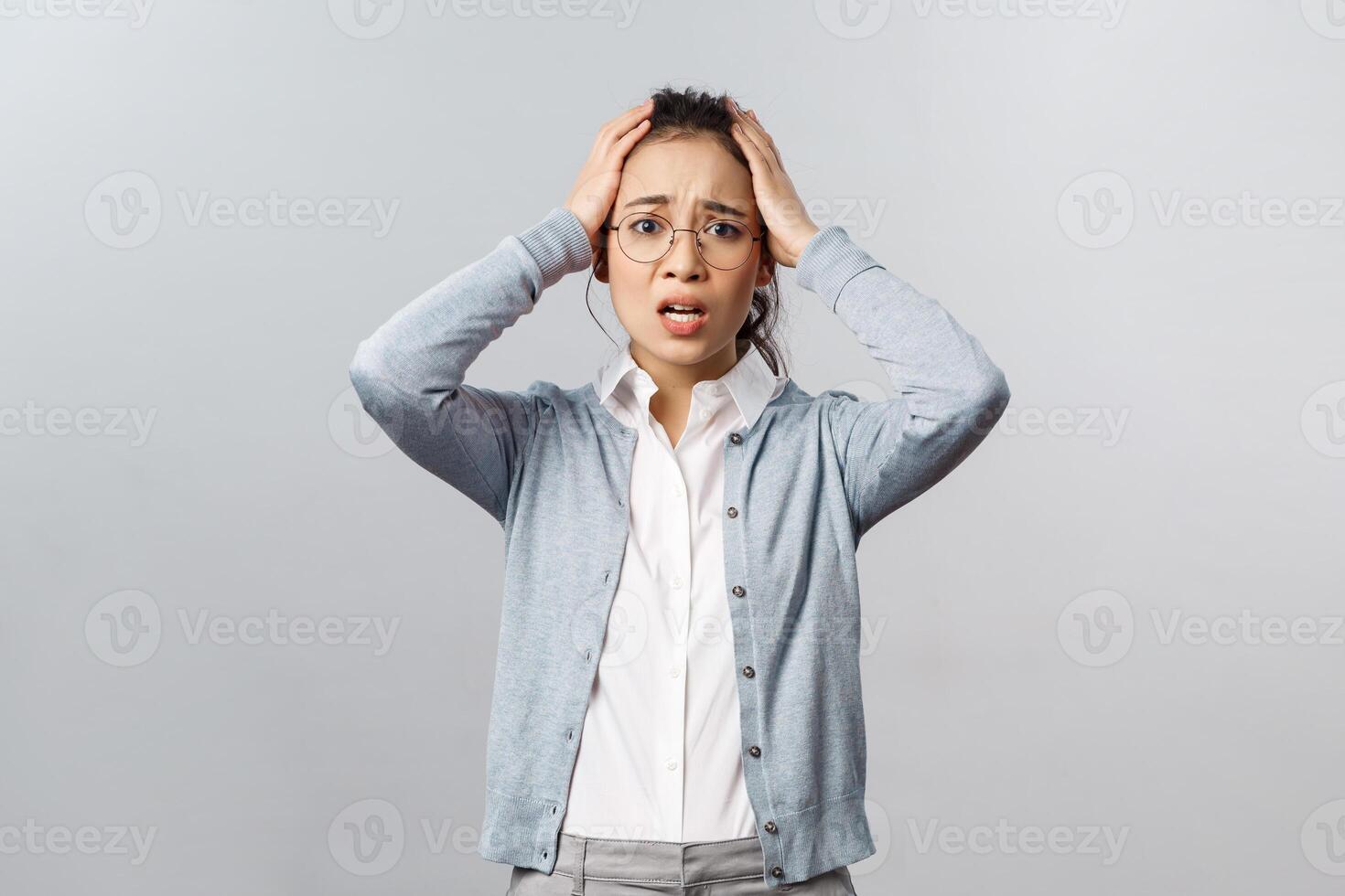 Emotions, people and lifestyle concept. Asian girl in panic, grab head dont know what to do, standing indecisive and desperate grimacing alarmed, have big trouble, stand concerned grey background photo