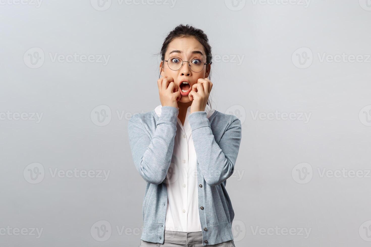 Emotions, people and lifestyle concept. Scared, startled asian woman gasping horrified, screaming, holding hands near mouth and staring with popped eyes at something frightening and scary photo