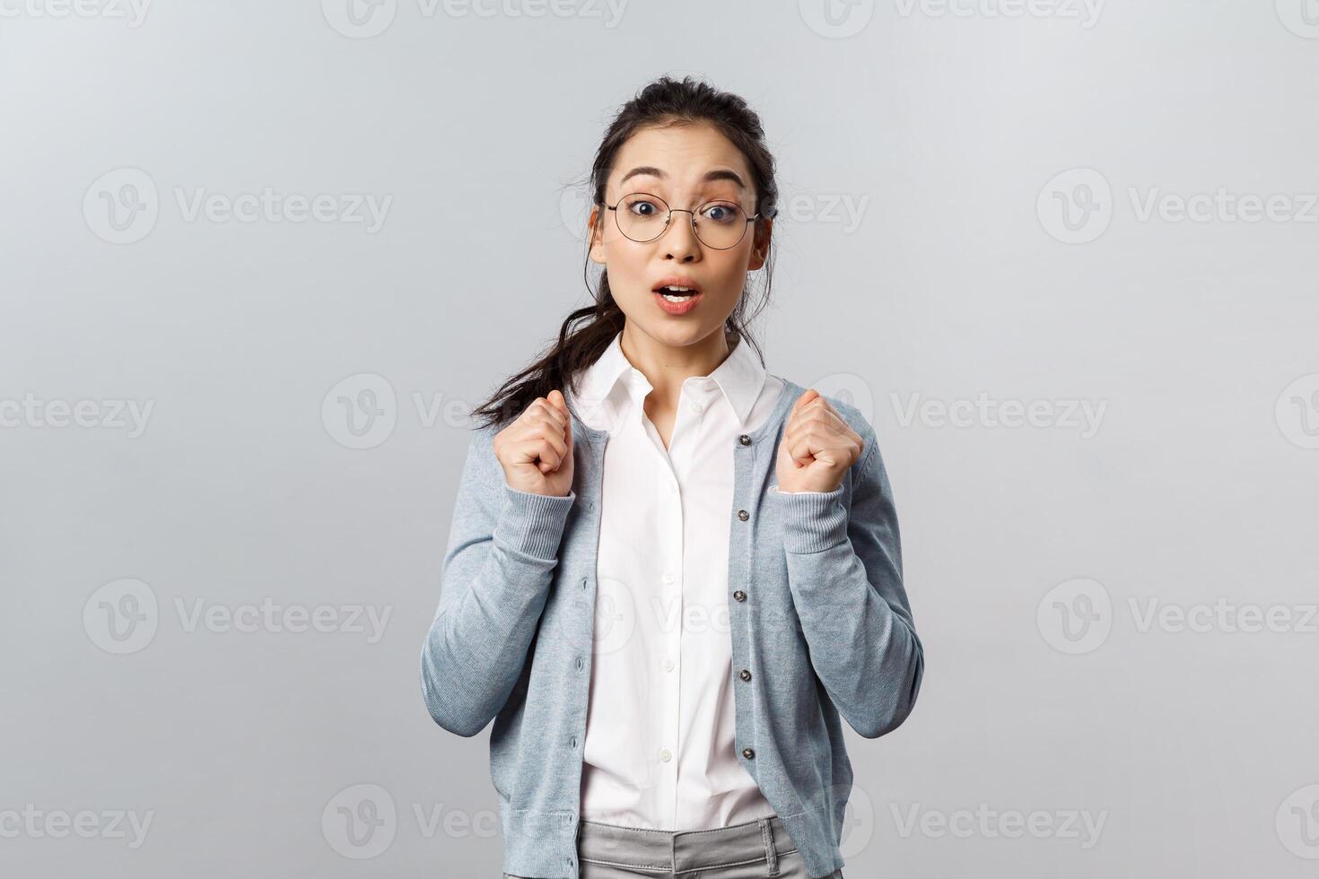 Portrait of excited and tempting cute asian girl in glasses, awaiting with thrill and interest for new season of favorite tv show coming up, looking ancitipation and amusement, stand grey background photo