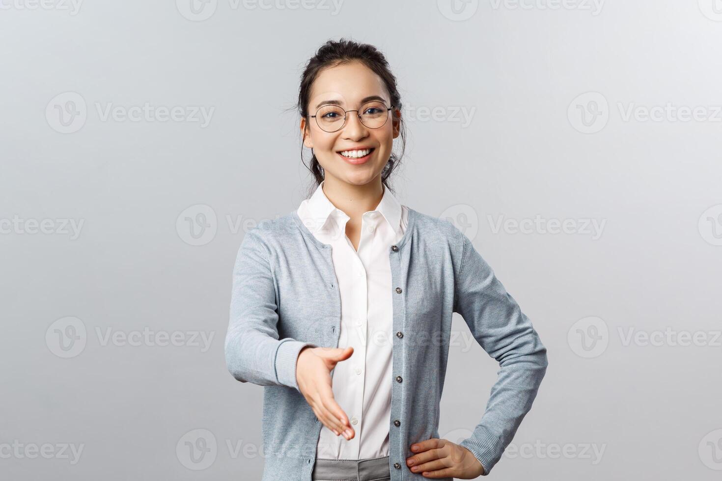 Lifestyle, people and emotions concept. Nice to meet you. Portrait of enthusiastic smart young woman in glasses, greet business partner, extend hand for handshake during meeting, grey background photo