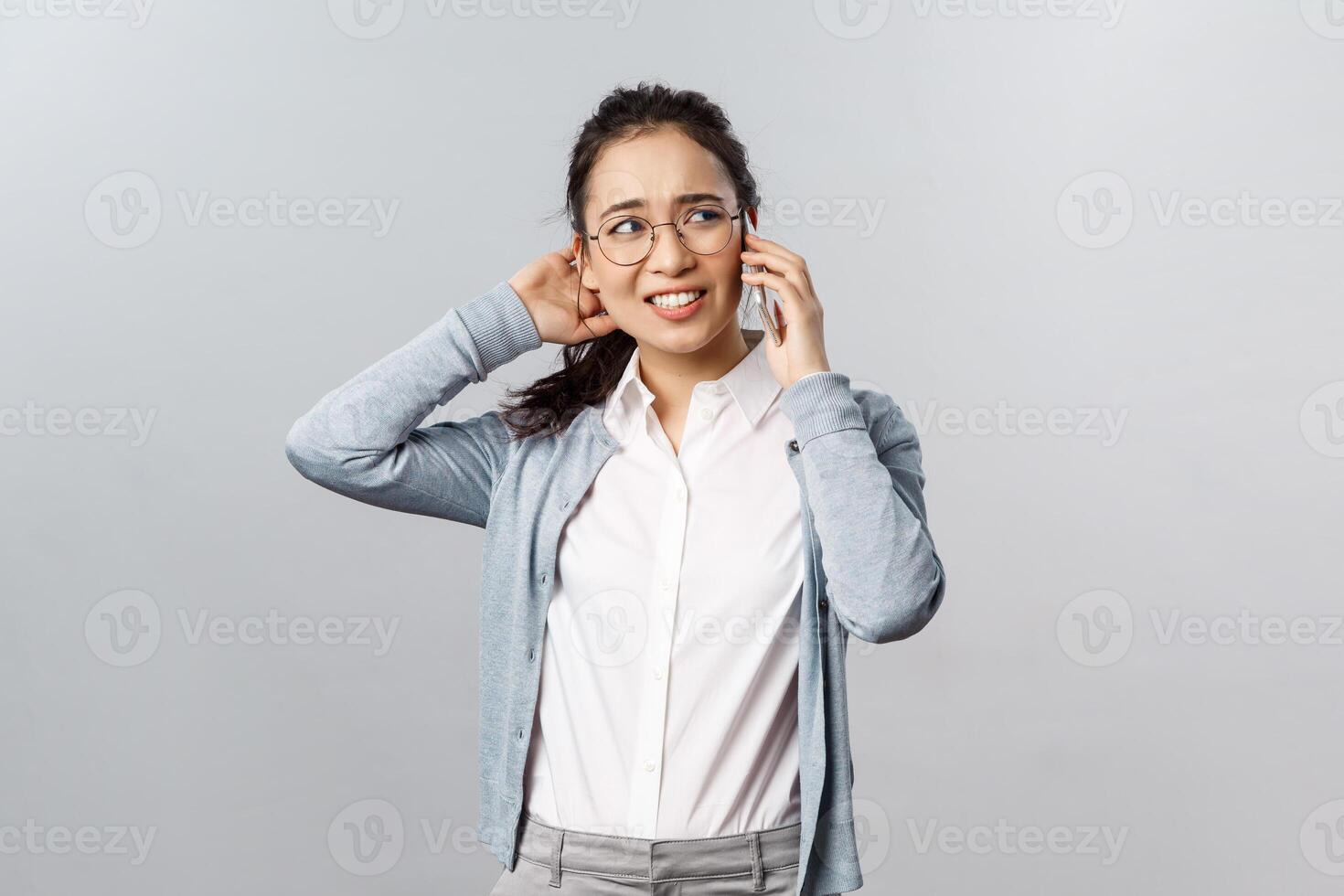 Office lifestyle, business and people concept. Reluctant unsure asian girl scratch back of head indecisive, have phone conversation, looking away troubled, feel awkward as rejecting offer for date photo