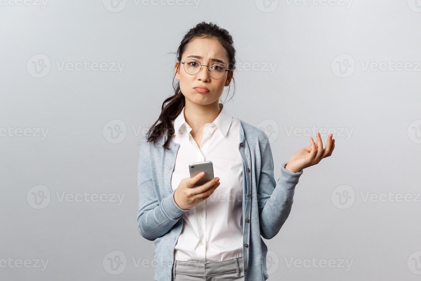 Office lifestyle, business and people concept. Gloomy indecisive and puzzled asian woman having proble, shrugging troubled and unsure, sighing, cant figure out how answer on message, use mobile phone photo