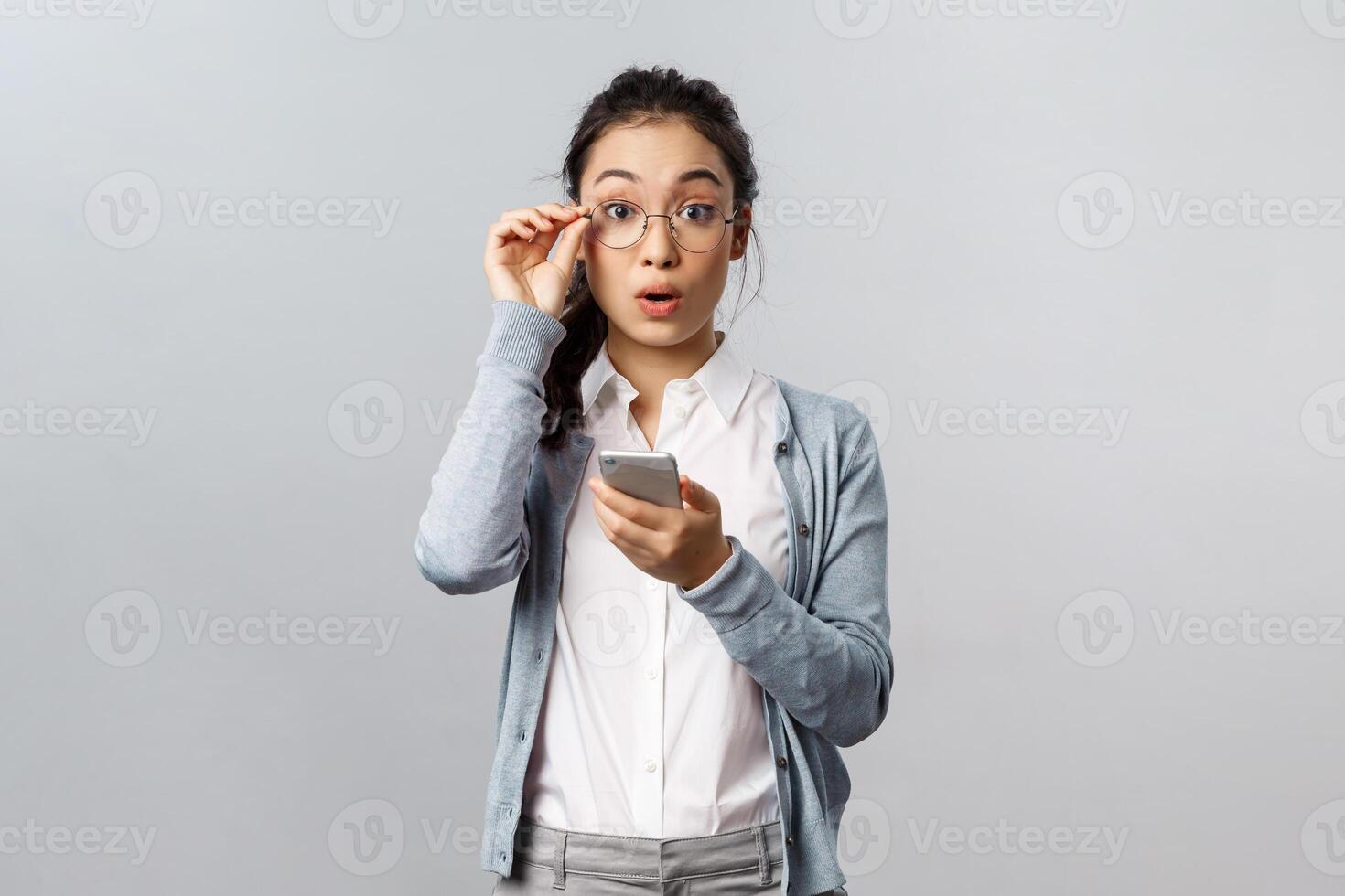 Office lifestyle, business and people concept. Very good. Impressed young asian female fixing glasses on nose, look surprised and amazed camera as using new app on mobile phone or receive text photo
