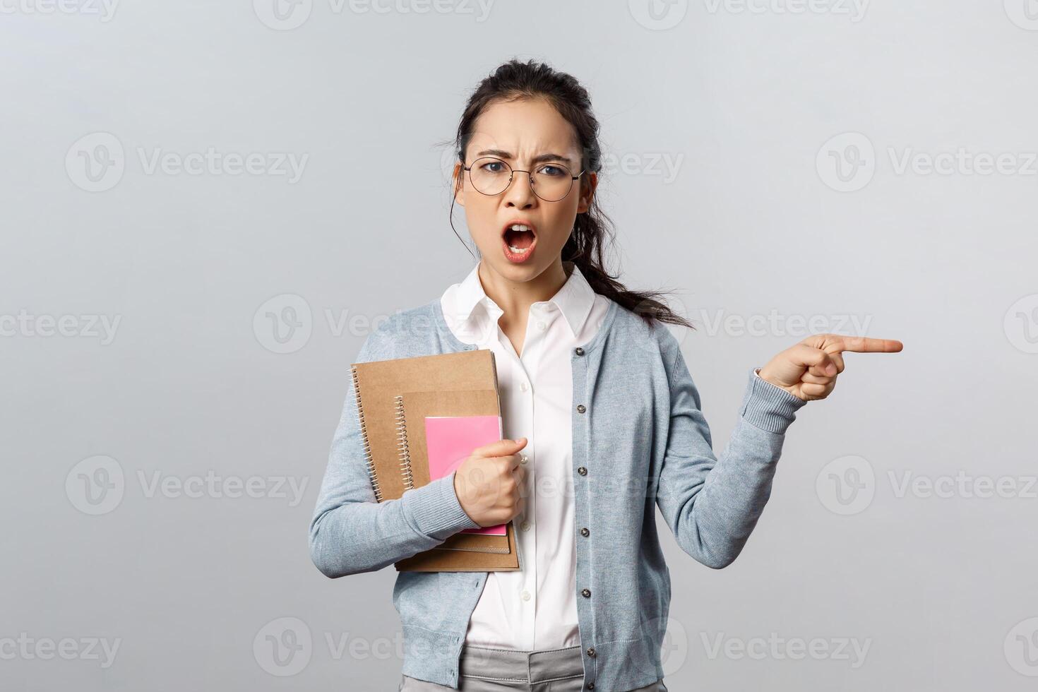 Education, teachers, university and schools concept. Angry and displeased strict tutor, teacher scolding student and tell leave class now, pointing at door shouting annoyed, grey background photo