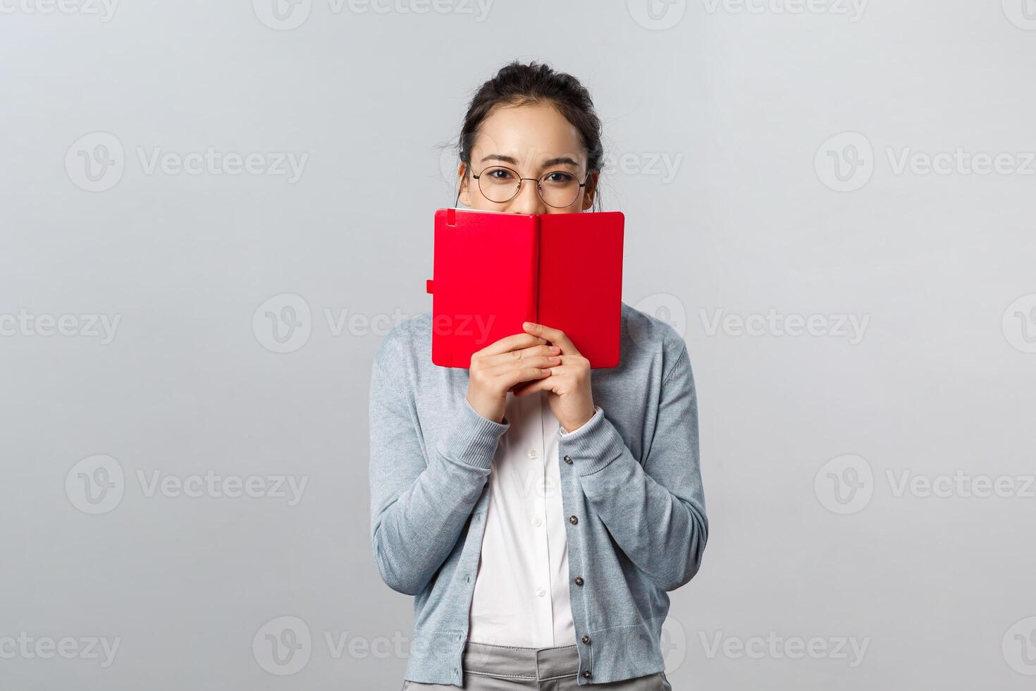 Teaching, education and university lifestyle concept. Silly blushing asian girl hiding her face behind diary, holding notebook or planner, hiding something she wrote from people, smiling with eyes photo
