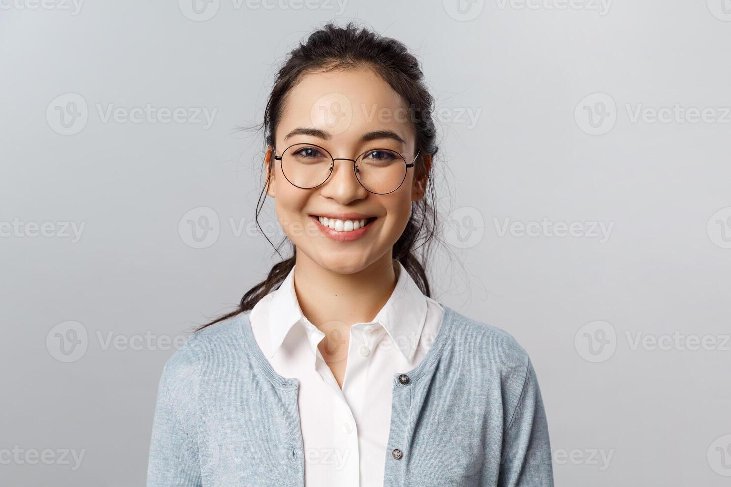 Close-up portrait of attractive, friendly-looking asian female office worker, employee or teacher in glasses, smiling broadly camera with enthusiastic attitude, stand grey background photo