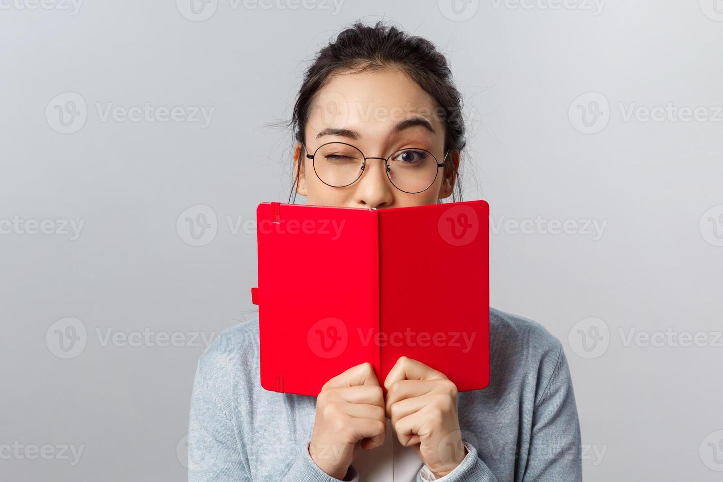 Education, university and people concept. Close-up portrait of cheeky female asian student, wink encourage classmates they pass exam, hiding mouth behind planner, studying, writing secret diary photo