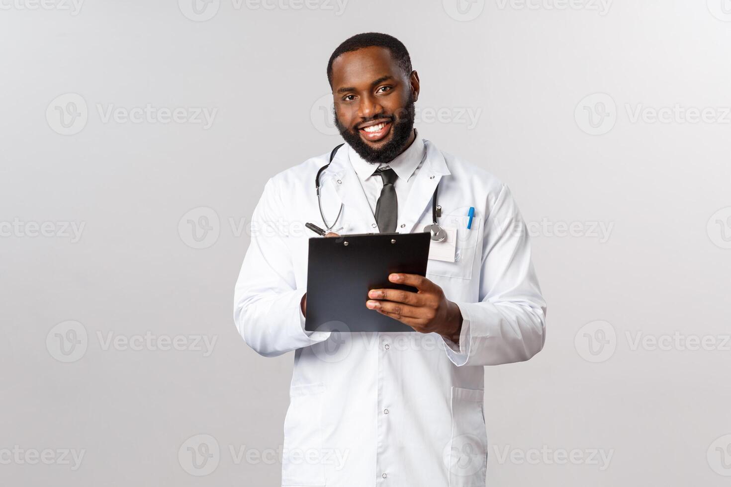 Medicine, covid19, treatment and hospital concept. Handsome african-american doctor treating patient, listening to person diseasy or symptoms, writing down clipboard during check-up photo