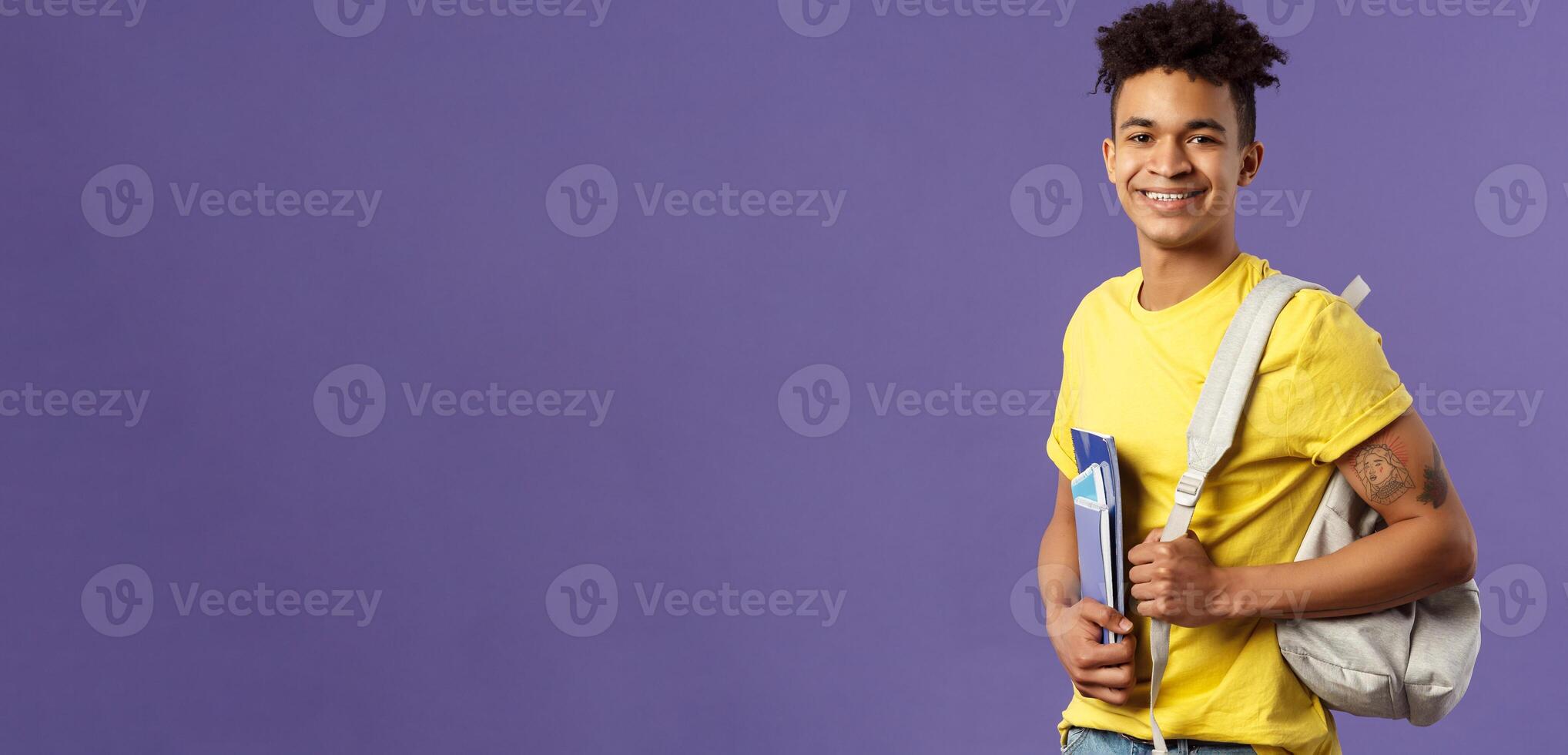 Back to school, university concept. Portrait of handsome charismatic hispanic guy, student walking to campus, going for lecture, studying hold backpack and notebooks, stand purple background photo
